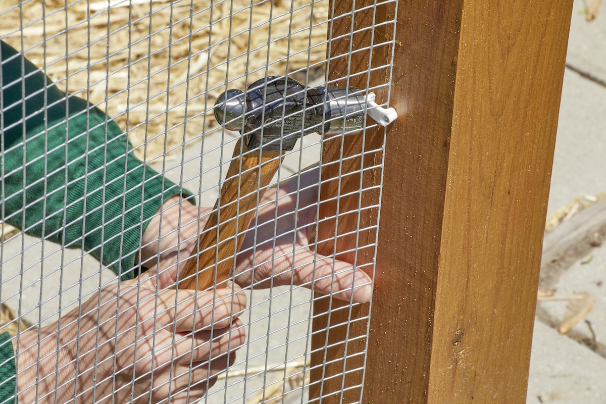 Woman hammers in clip holding fence wire into fence post.