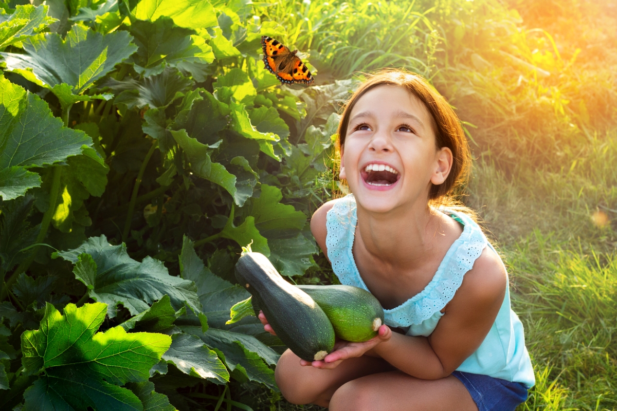 Girl smiling at butterfly holding zucchini