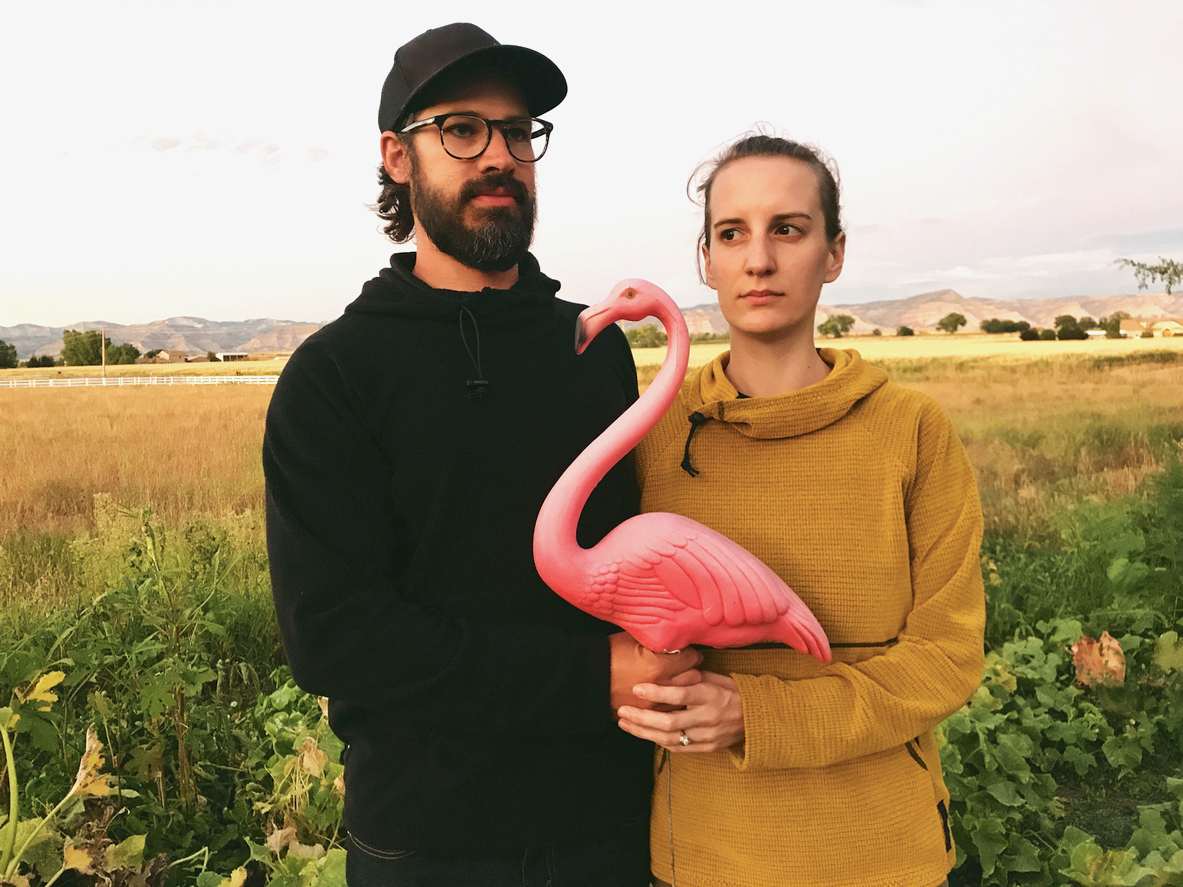 a-young-man-and-woman-in-a-field-hold-a-plastic-pink-flamingo-in-the-same-post-as-the-painting-American-Gothic