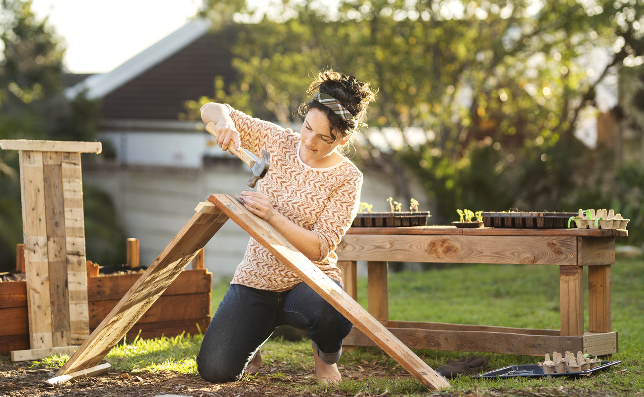 Young woman building a planting box while working outside in her backyard on a sunny afternoon