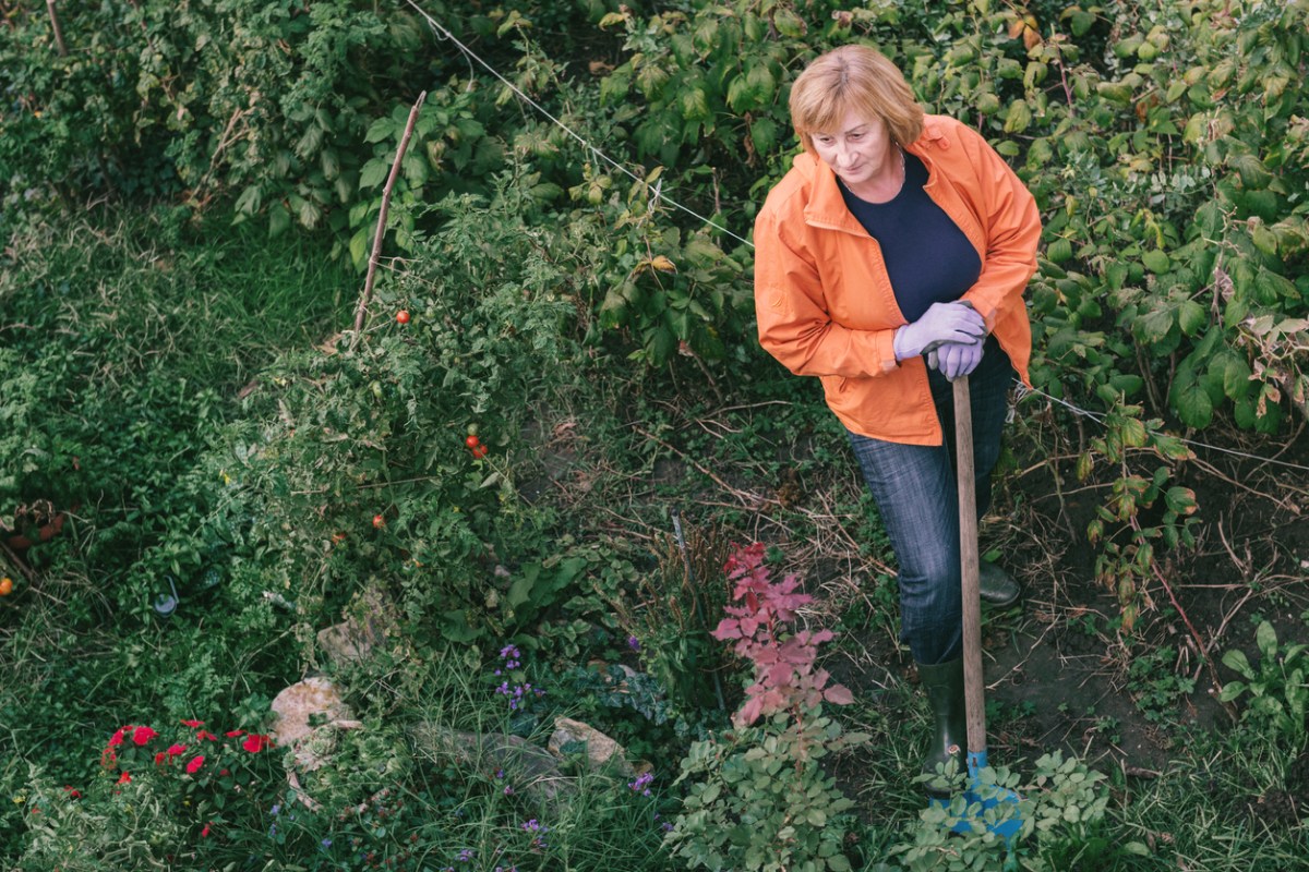 woman-stands-in-a-garden-of-various-plants-with-a-shovel