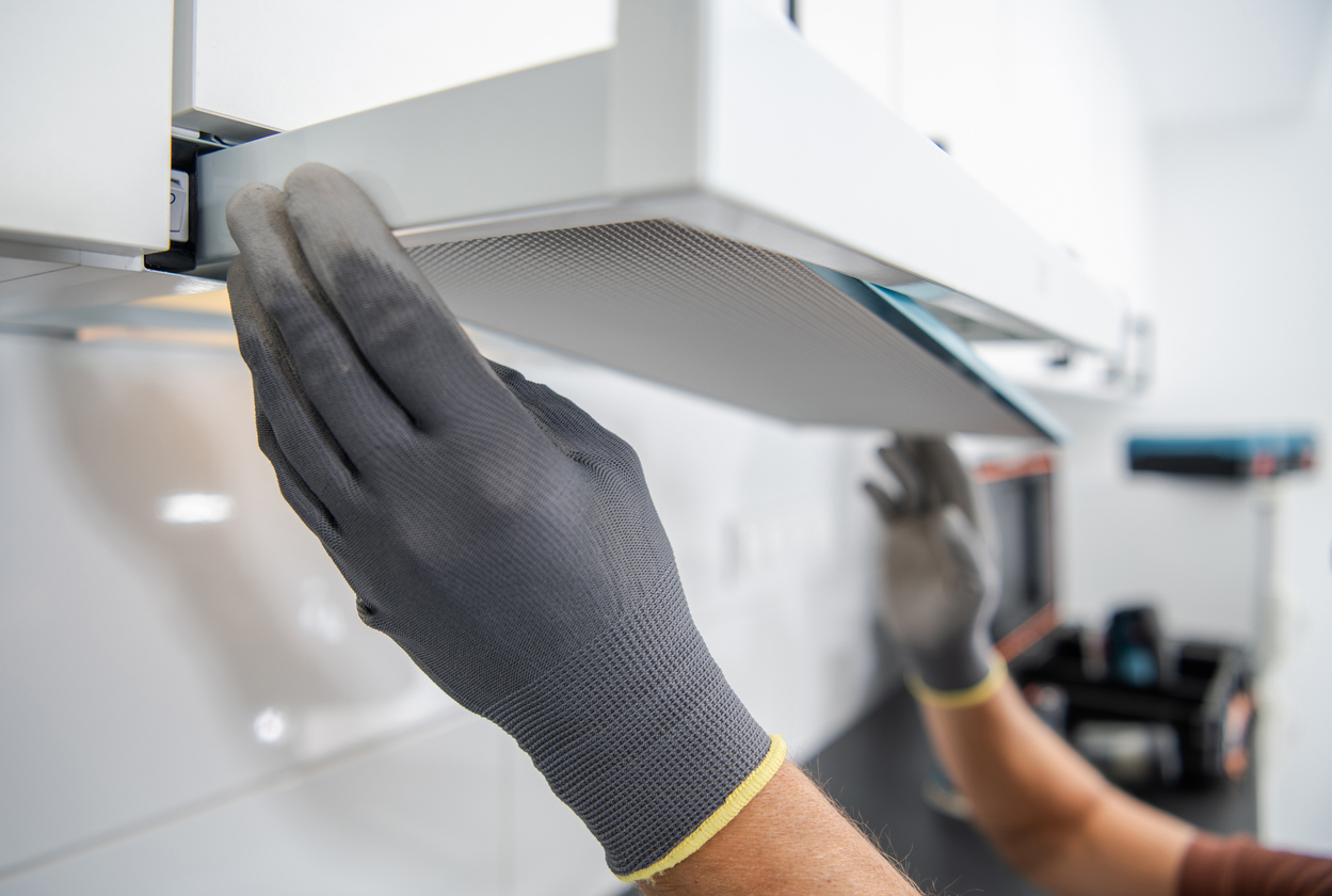 close up of range hood filter being removed by two hands with grey gloves