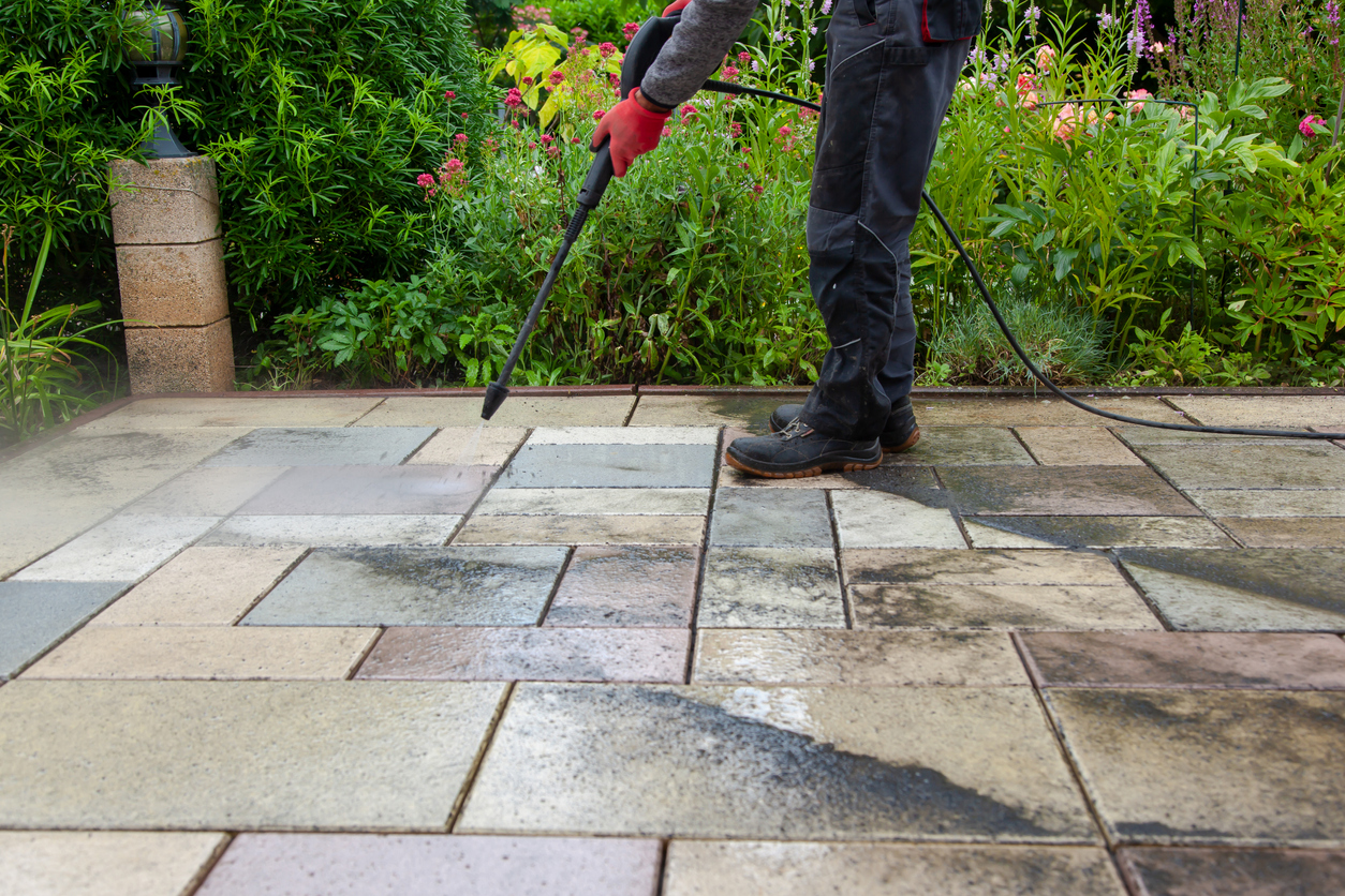 man-from-the-waist-down-is-power-washing-flagstones-on-a-patio-near-flowers