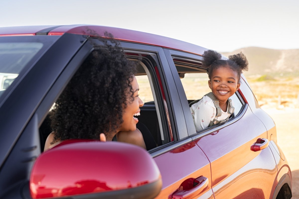 mother leaning out drivers side of window of red SUV looking at daughter in backseat window in desert landscape