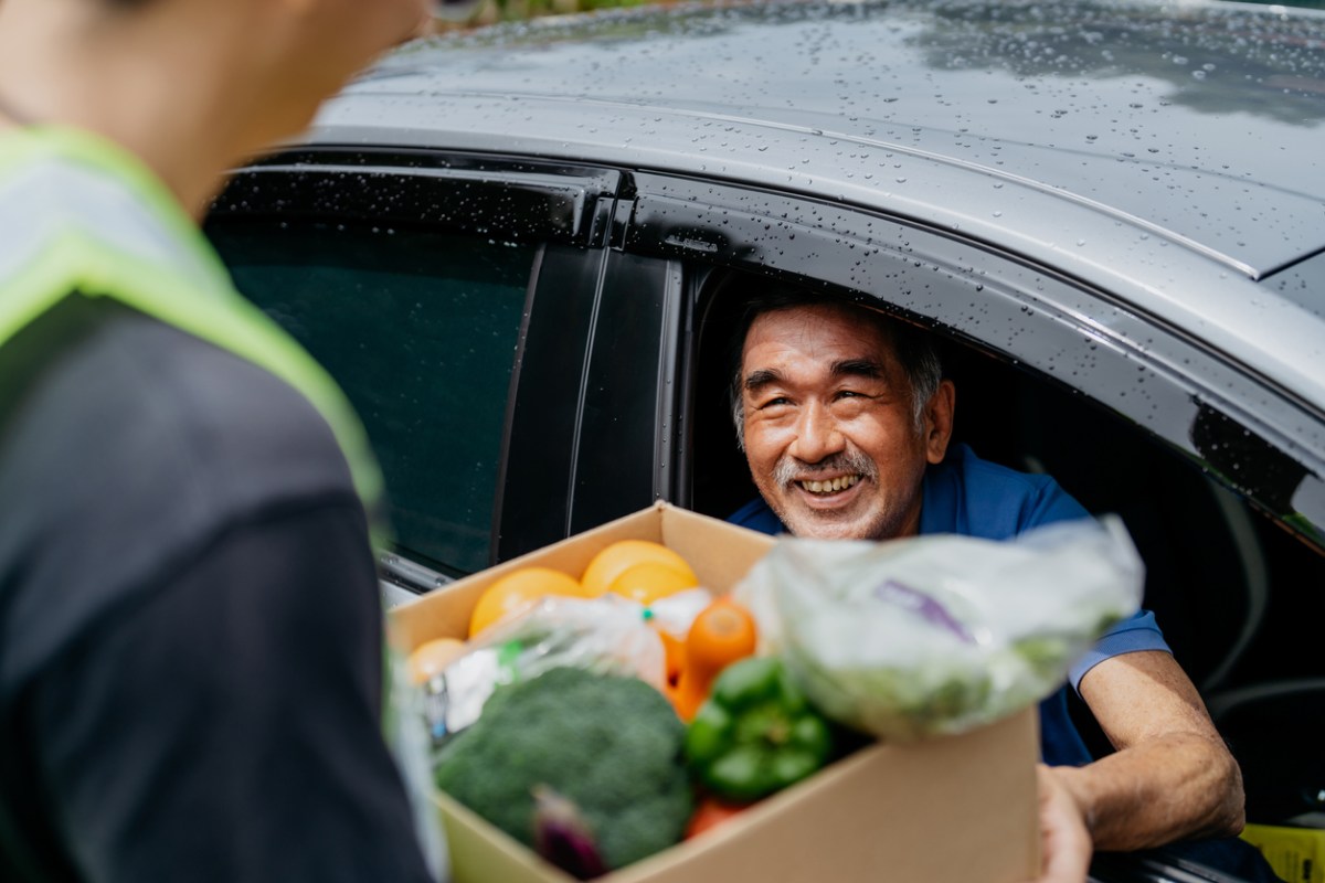 person-handing-a-box-of-fresh-produce-to-a-senior-man-through-his-car-window