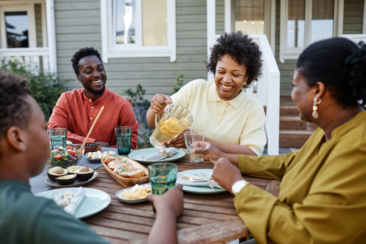 Portrait of smiling black woman pouring lemonade drinks to glass during family gathering outdoors
