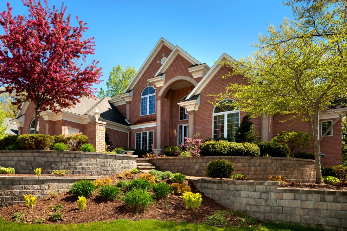 large brick house with tried stone wall landscaping and bright trees and bushes