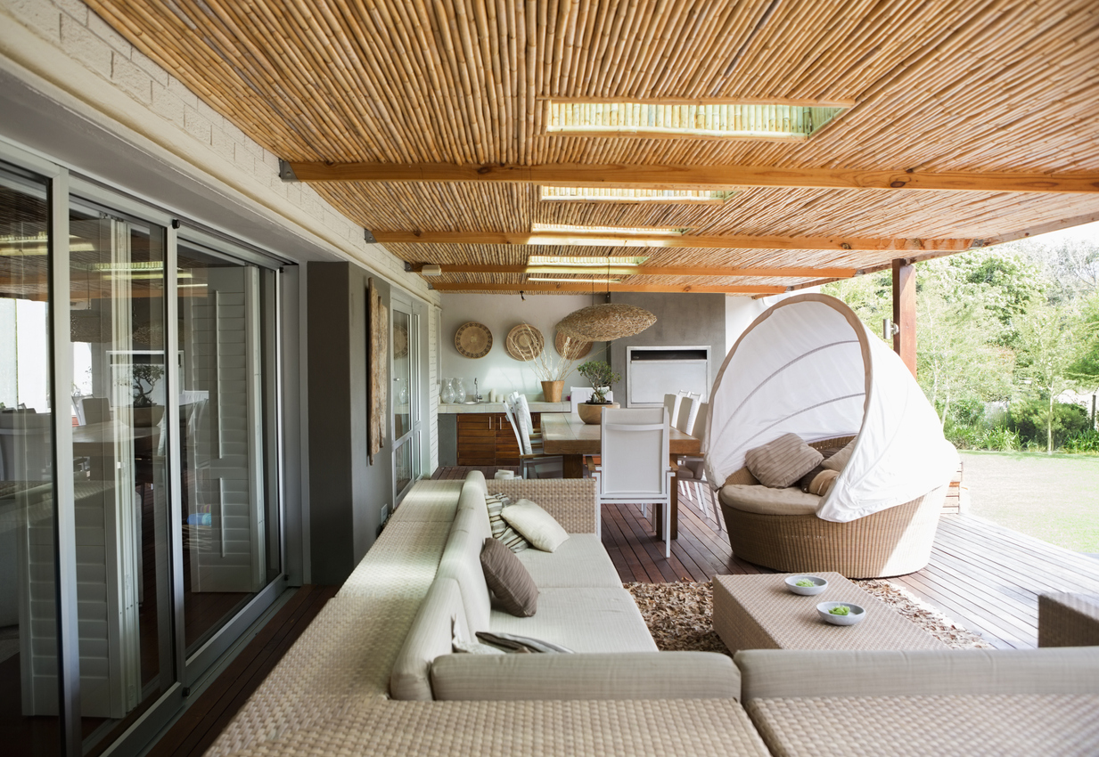 side view of sunroom with bamboo roof and large patio furniture with one open wall and two visible closed walls with entrances and windows