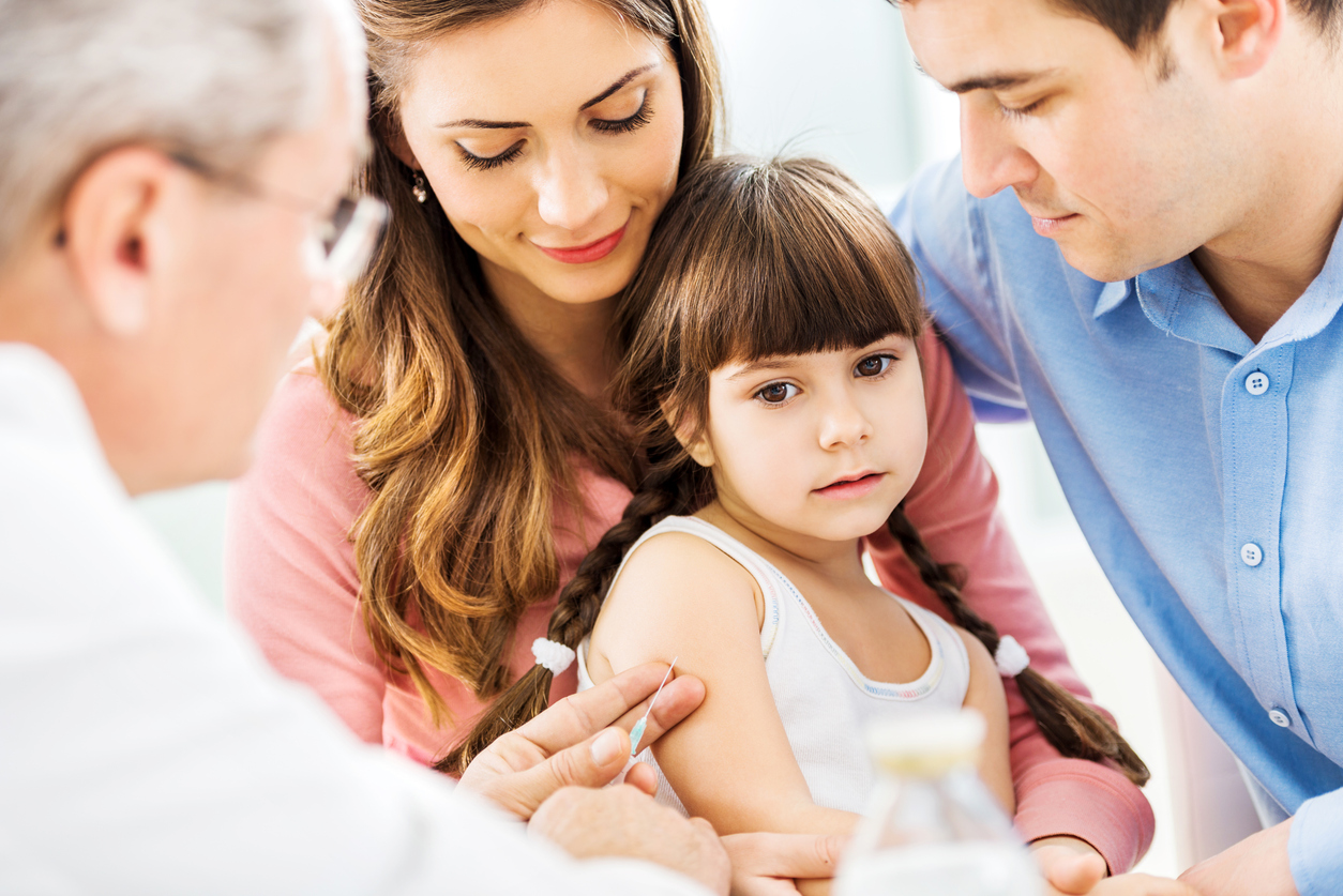 young girl with her parents getting vaccinated by doctor who aims needle at her arm