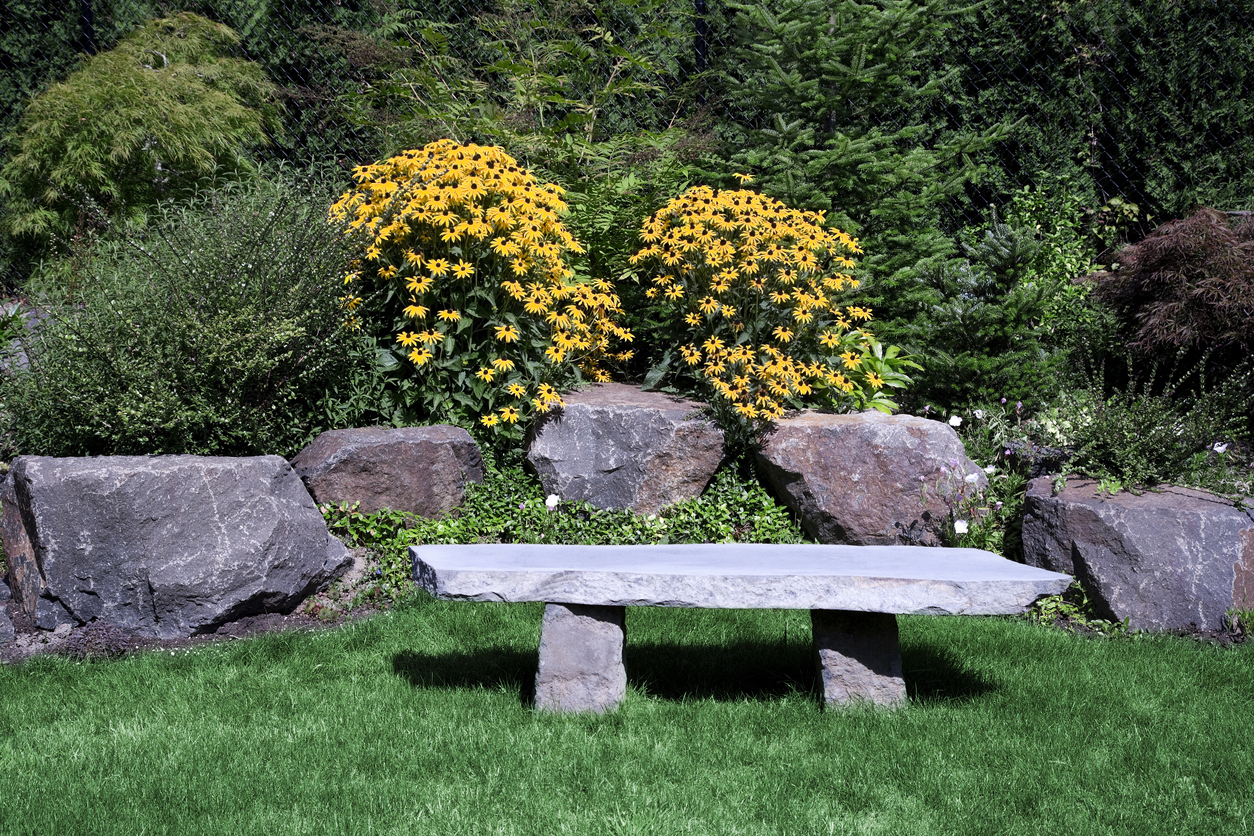 Basalt garden bench sitting in green yard with yellow flowers.