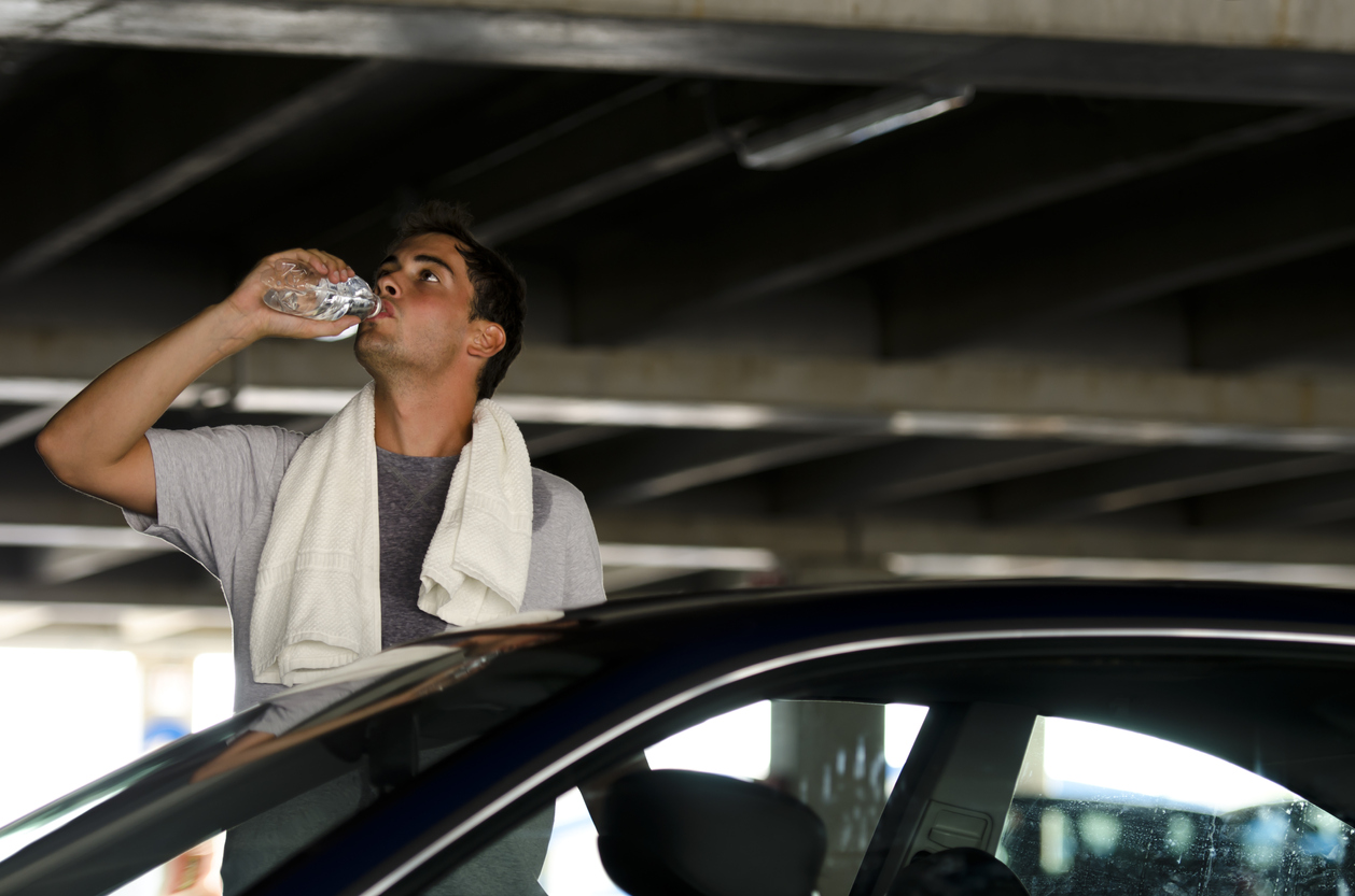 man standing outside of his car cooling off with towel and water bottle
