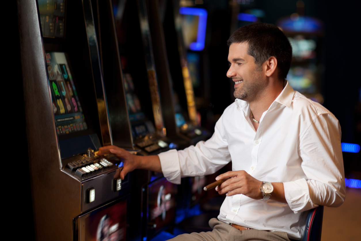 man in casino sits at slot machine smoking a cigar and smiling