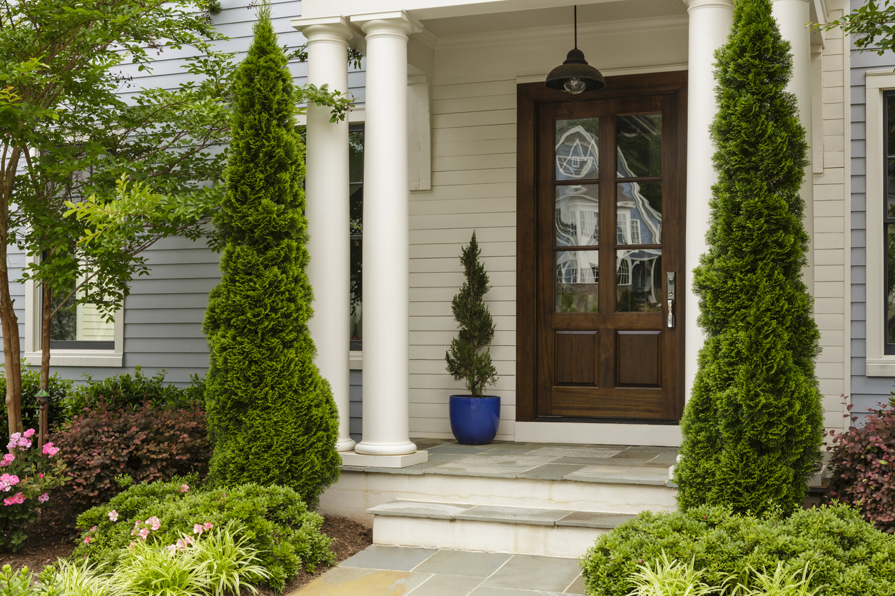 Side view of dark wood front door on elegant front porch with tall trees flanking porch and floral landscaping