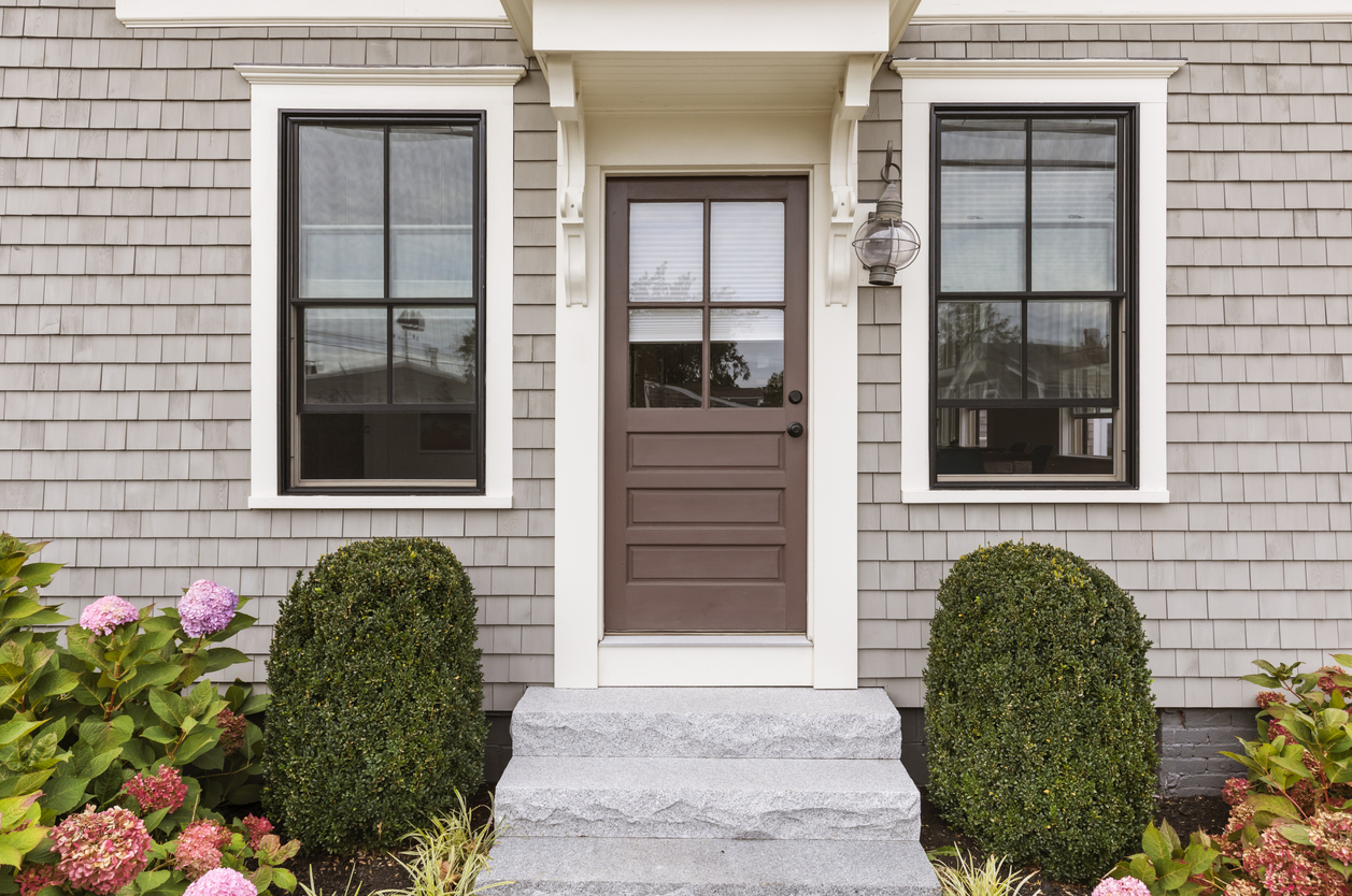 brown front door with white accent framing and two bushes creating symmetrical landscaping in front of house
