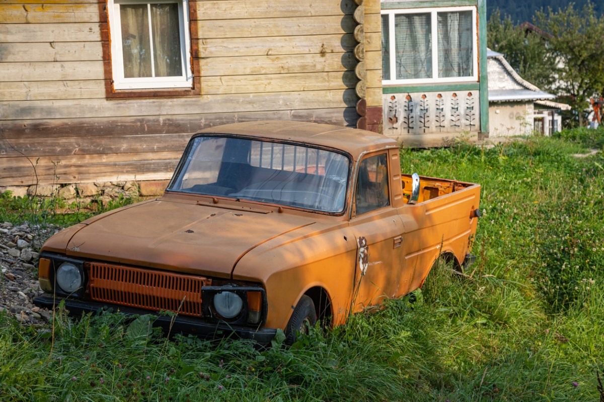 old orange car abandoned in yard of derelict house