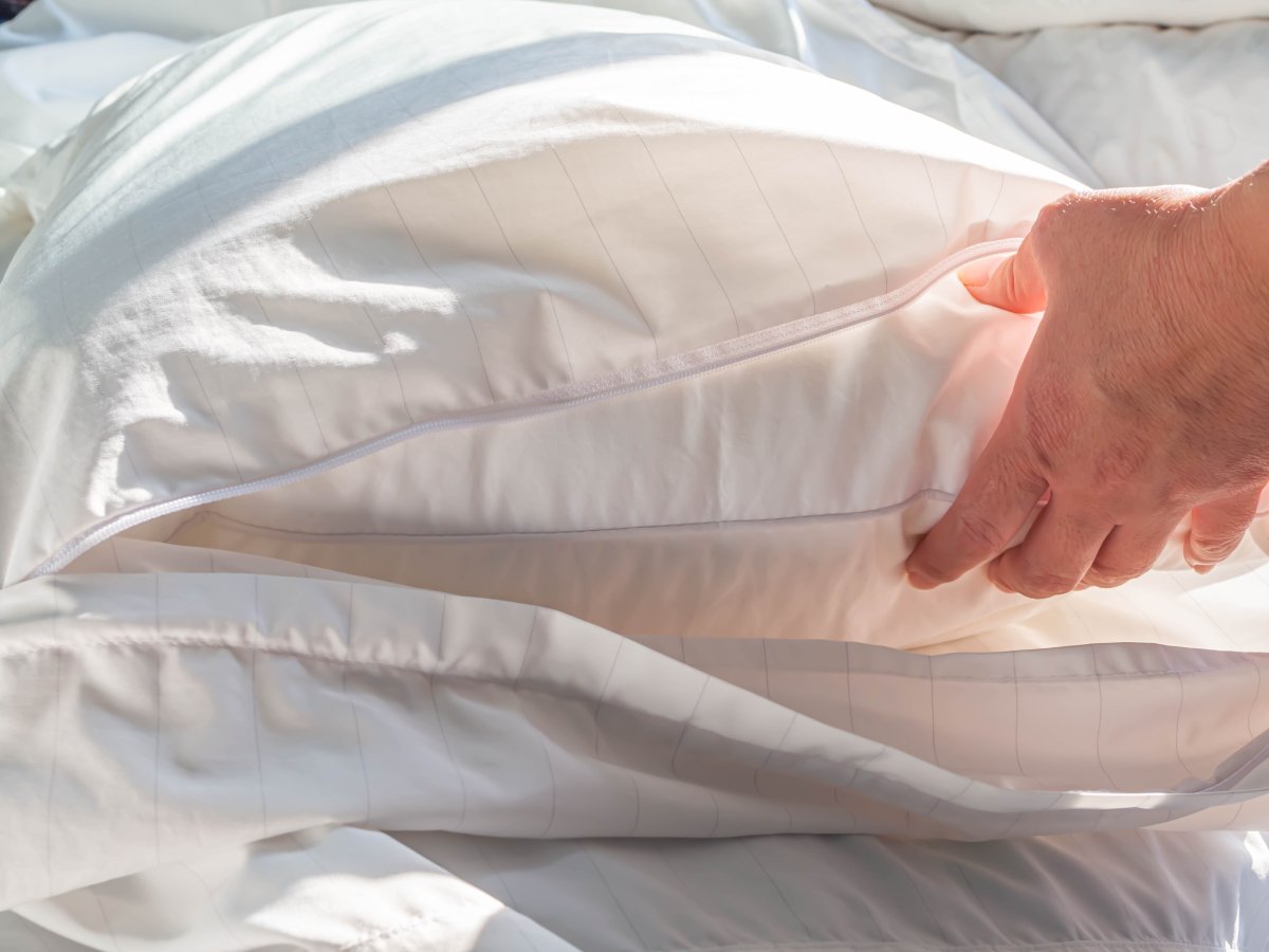 Person unzips a dust cover on a bed pillow and reaches in to remove the pillow.
