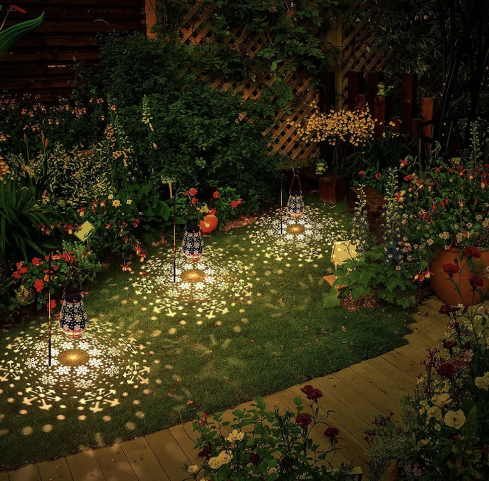 high angle view of backyard at night with colorful flowers and hanging lanterns casting snowflake patterns on the lawn