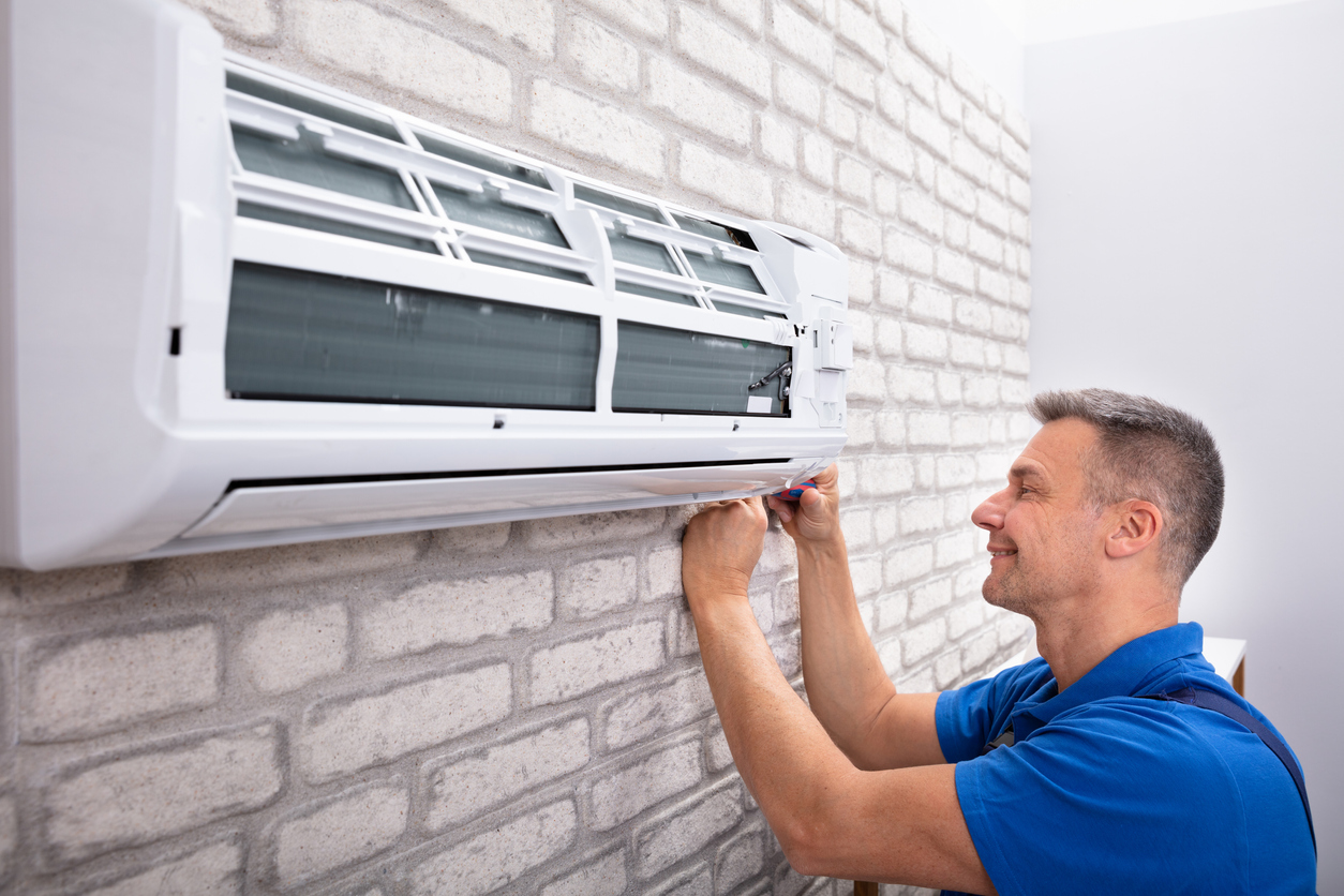 A person making an adjustment on the best garage air conditioner option installed through a brick garage wall