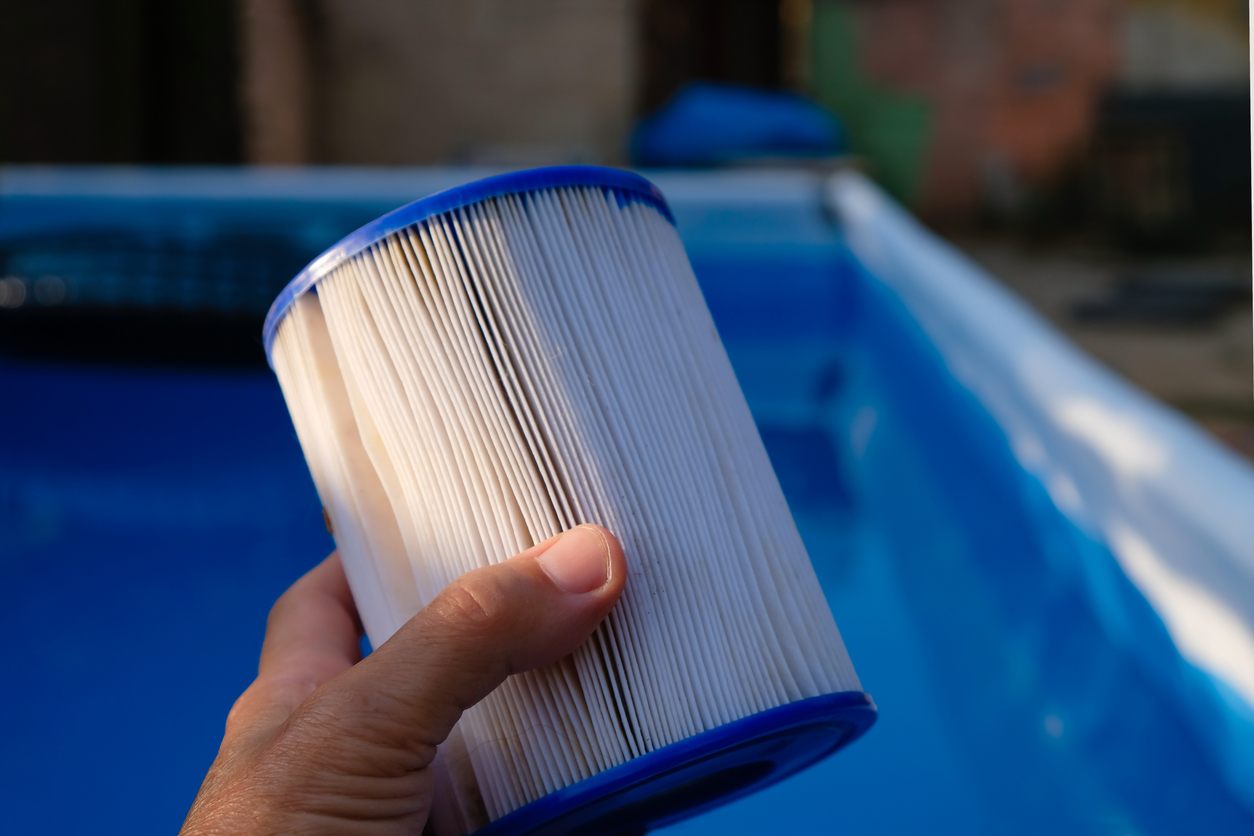 Hand holding a clean pool filter cartridge over an above-ground swimming pool