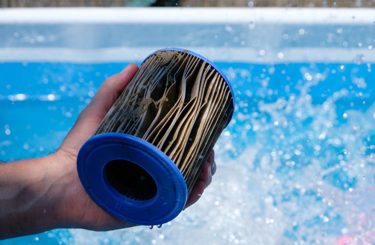 Dirty pool filter cartridge held over splashes coming from a swimming pool