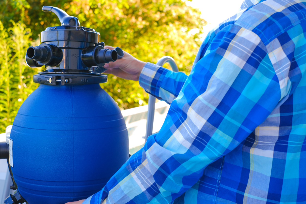Over-the-shoulder view of man setting up blue pool sand filter outdoors