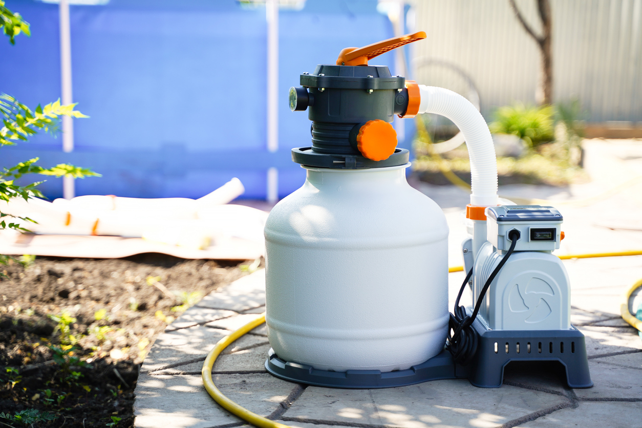 White and orange pool sand filter system next to an above-ground pool
