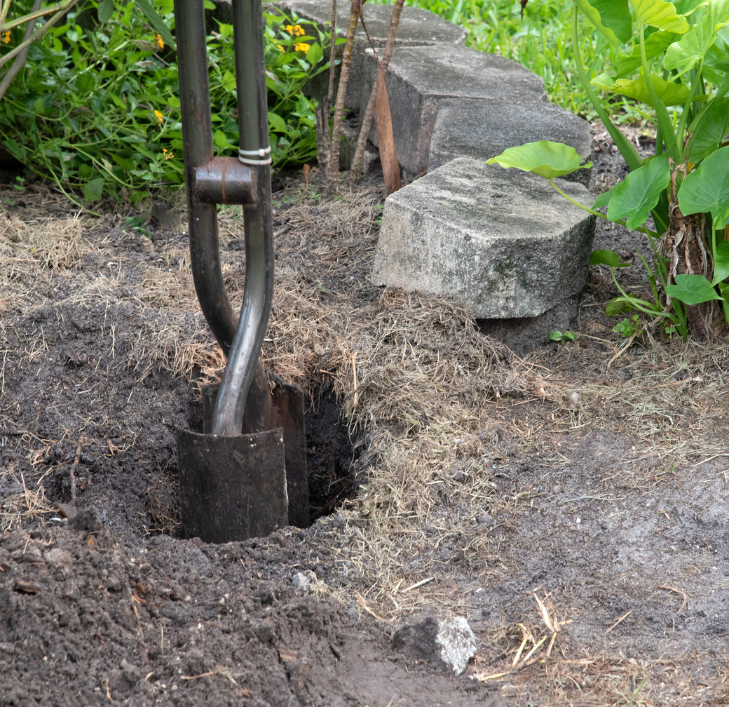 Post hole being dug in a home garden with a post hole digger