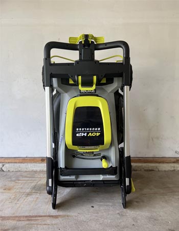 The Ryobi 21-inch self-propelled all-wheel-drive mower in a garage with its handle folded down for storage