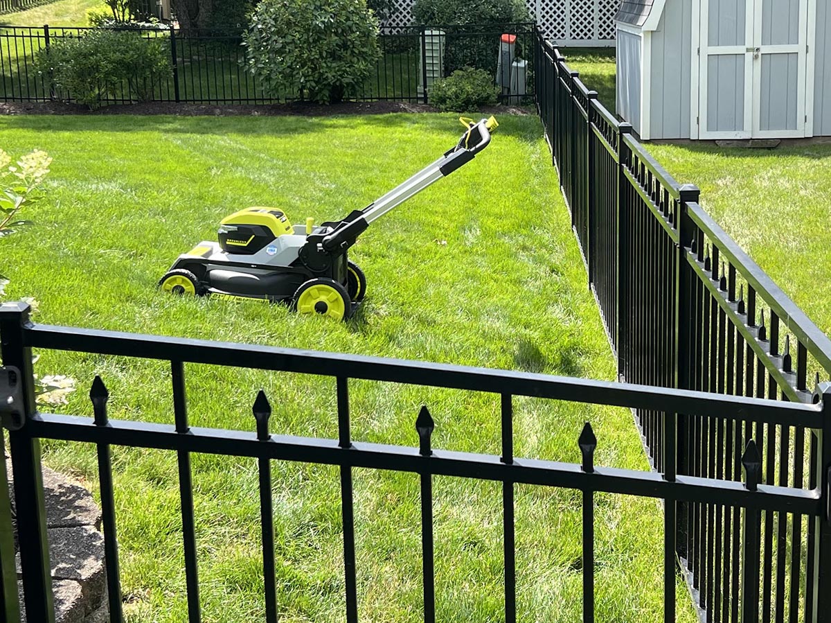 The Ryobi 21-inch self-propelled all-wheel-drive mower in the corner of a neatly trimmed lawn next to a fence