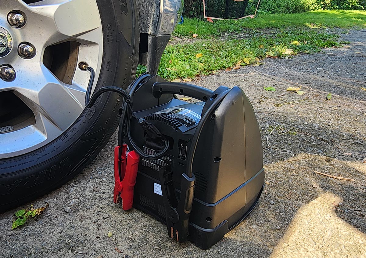 The Schumacher portable power station and jump starter on the ground next to a car tire that's being inflated