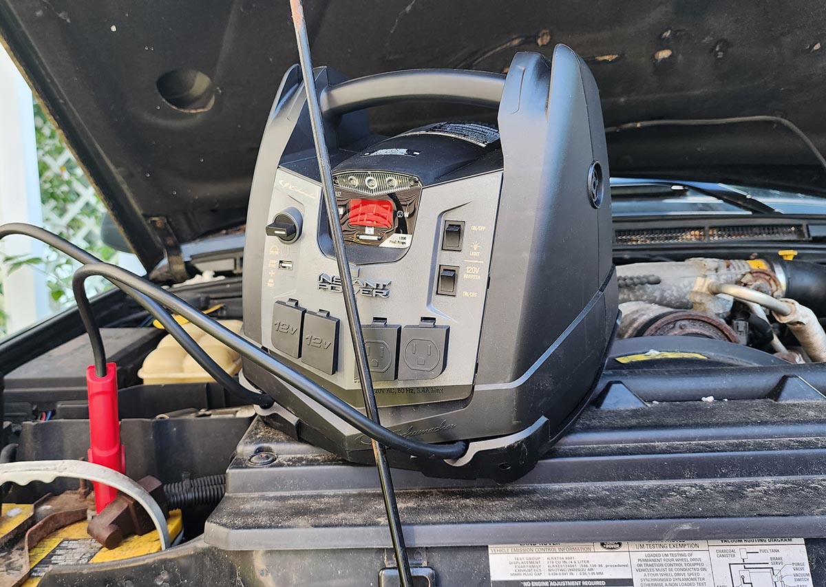 The Schumacher portable power station and jump starter sitting on a car engine while charging the car's battery