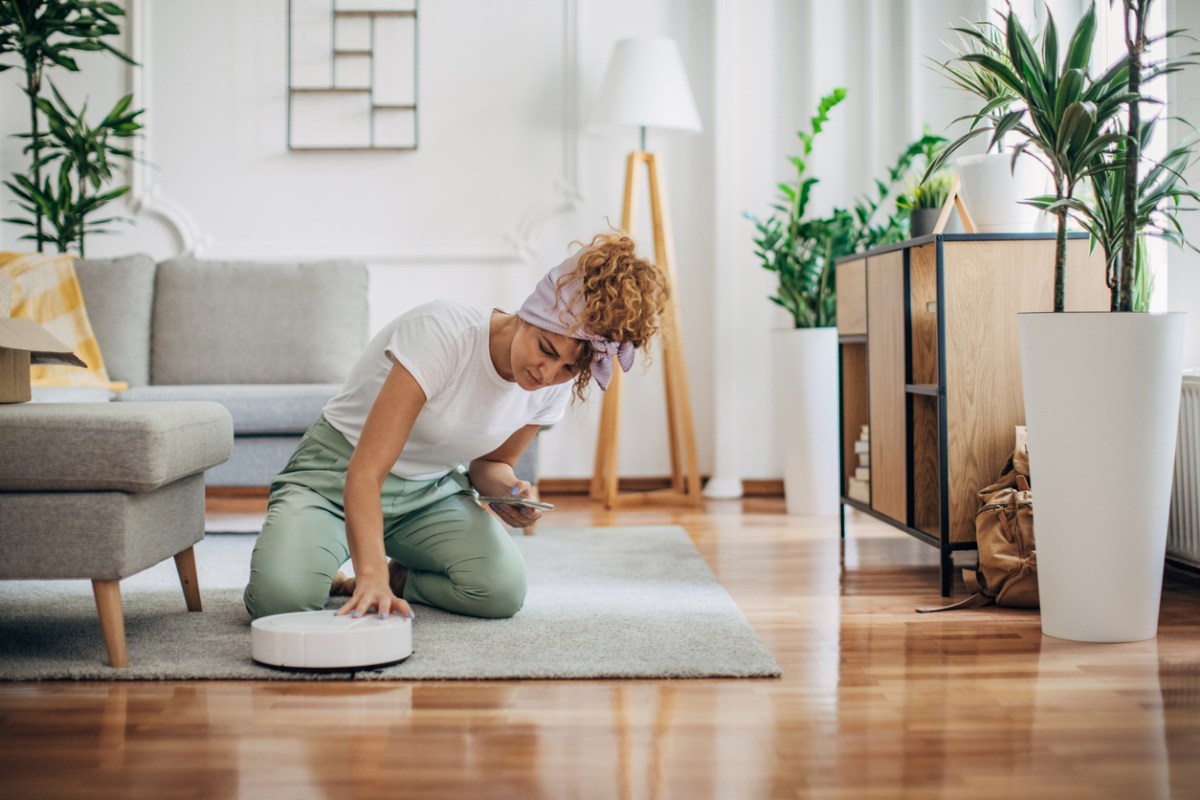 A woman making an adjustment to the best cheap robot vacuum that's sitting on a rug