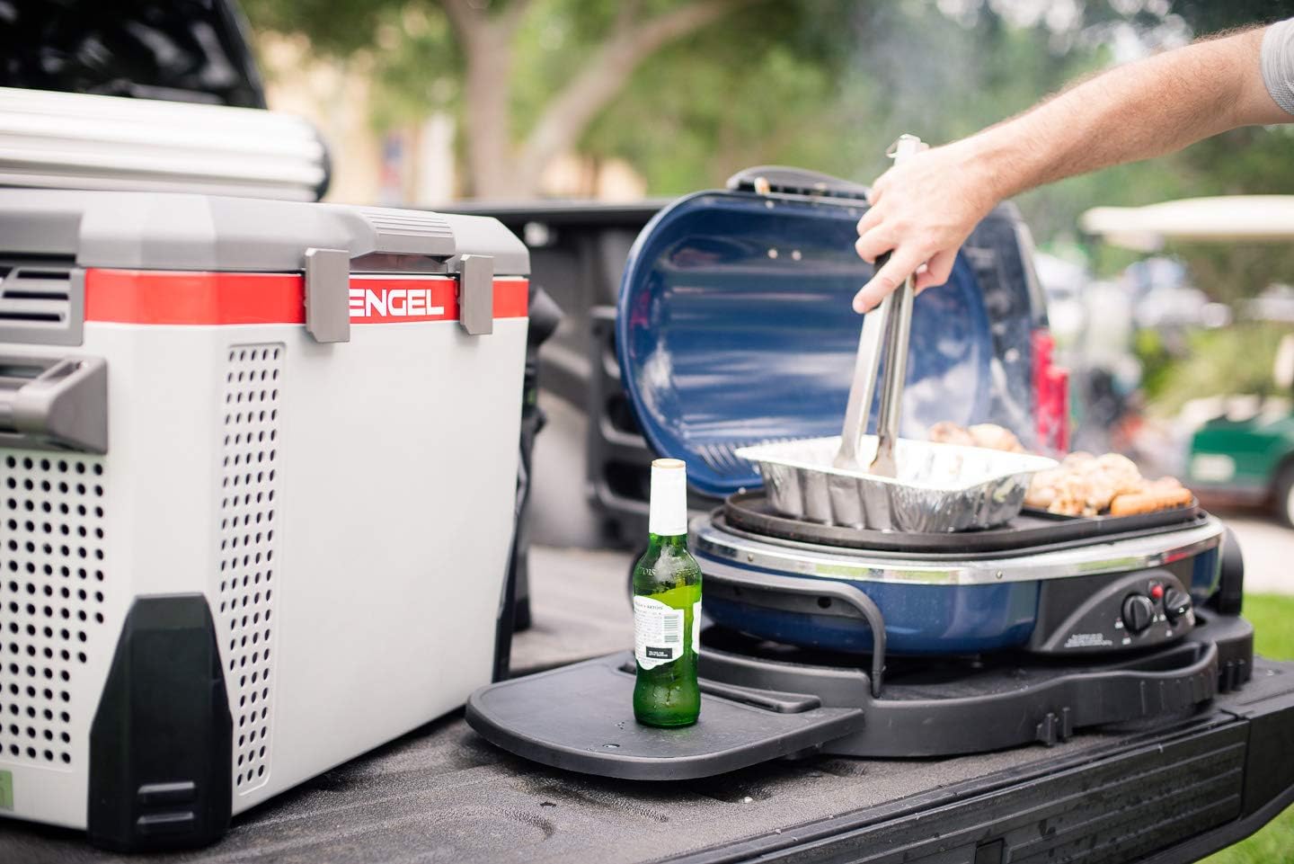 A close-up of a person grilling on a truck bed next to the best electric cooler option