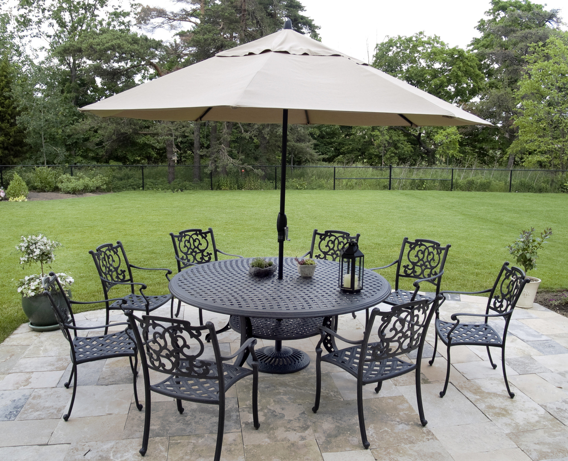 The best patio umbrellas for windy conditions option set up through the center of a metal patio set before a large grassy yard