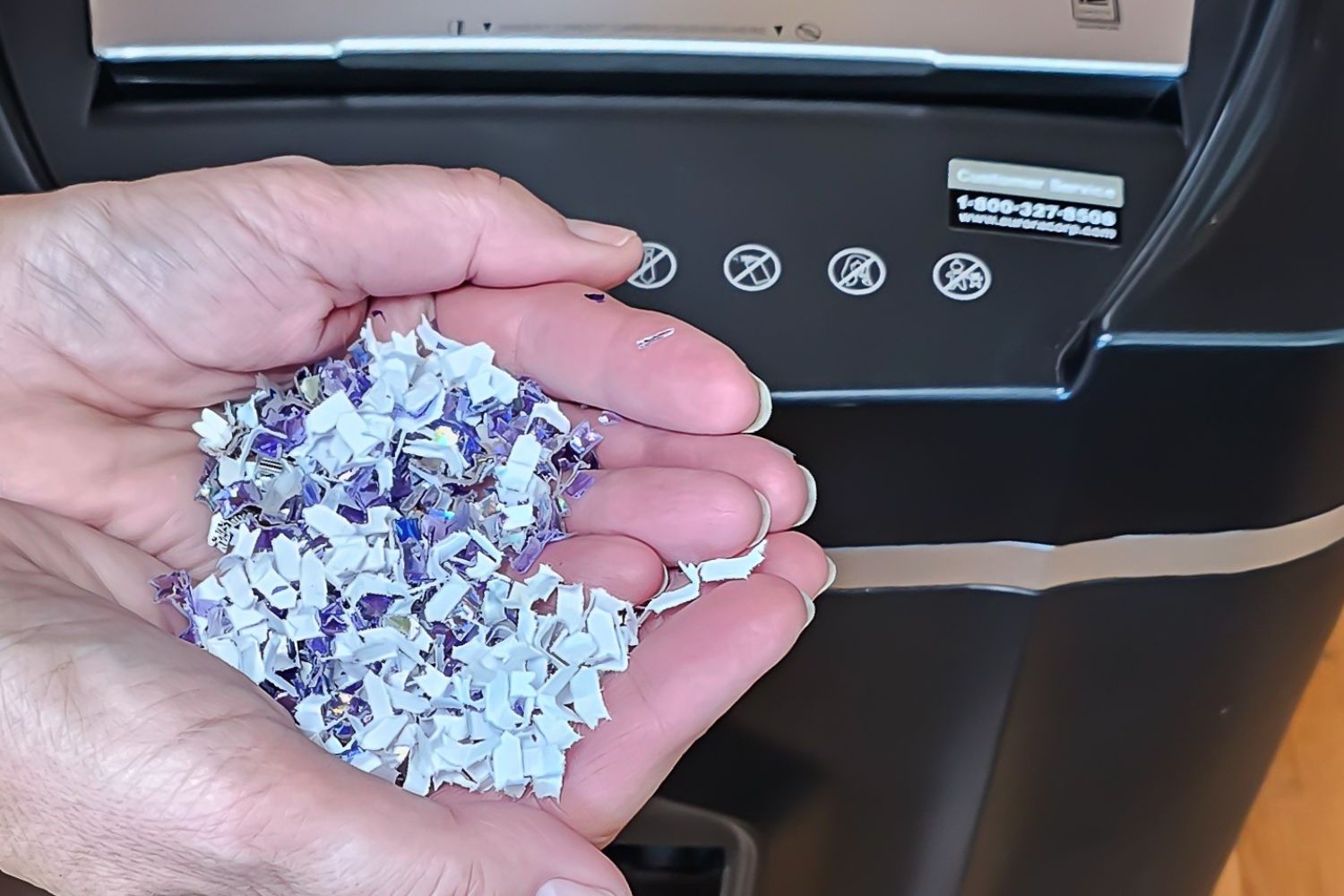 Cupped hands holding micr-cut paper waste just over the feed of the Aurora paper shredder