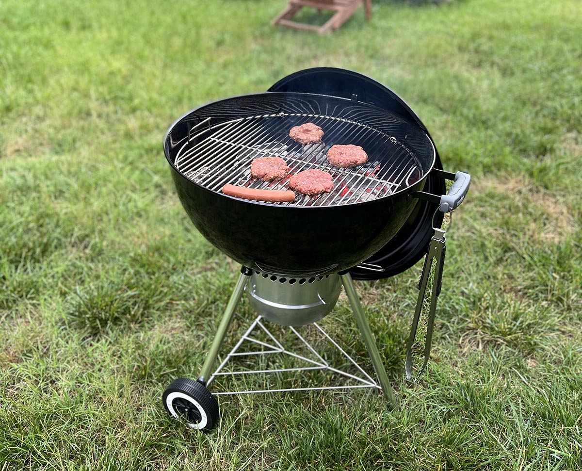 The Weber Original Kettle Premium charcoal grill in use grilling meat in a yard