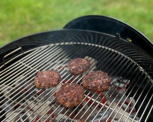 The Weber Original Kettle Premium charcoal grill in use grilling meat in a yard
