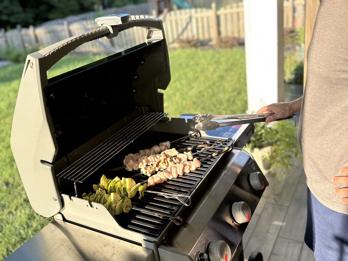 A person using tongs to flip food cooking on the Weber Spirit II E-310 Gas Grill