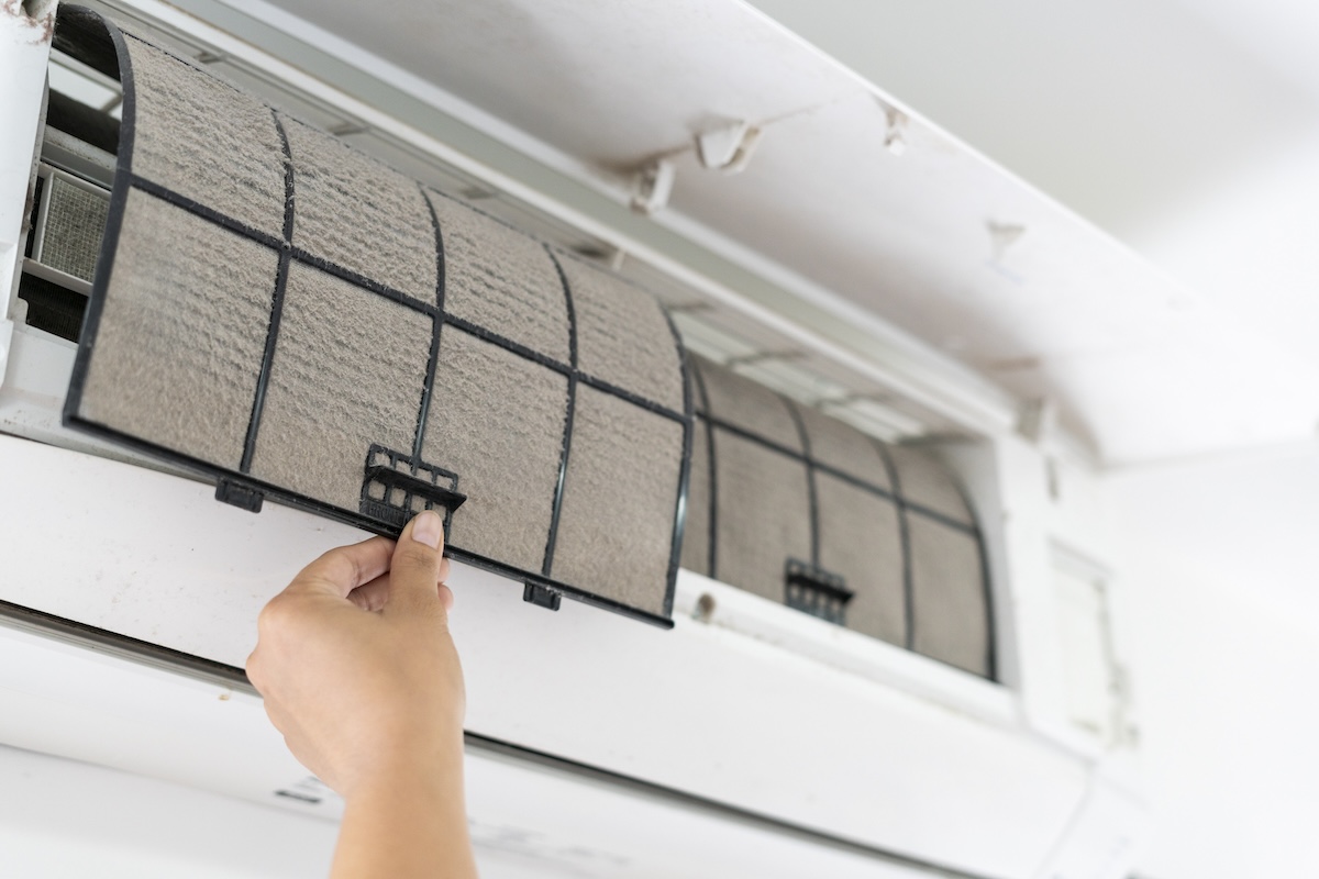 A set of hands pulls a dirty air filter out of the air conditioning unit.