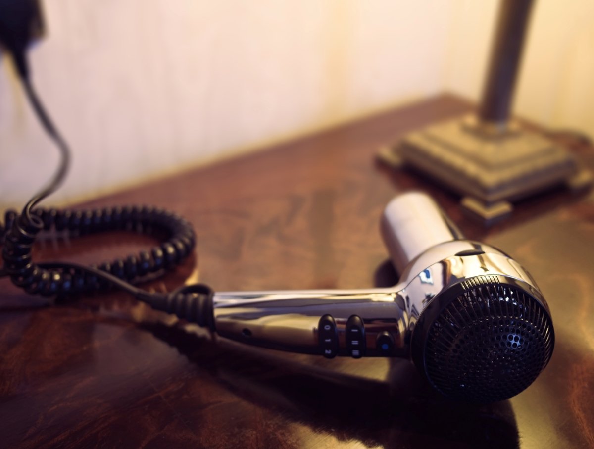 A black blow dryer lying on a table, near a lamp.