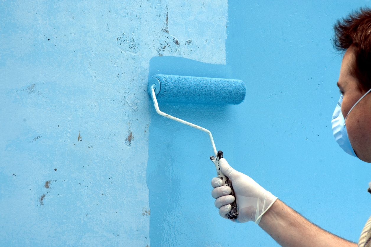 a man wearing a mask uses a roller to paint a wall blue