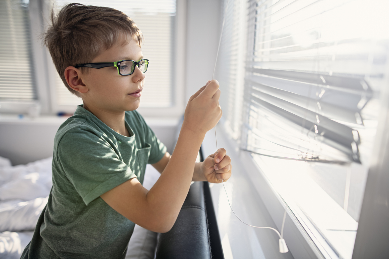 young boy having trouble opening the blinds on a window