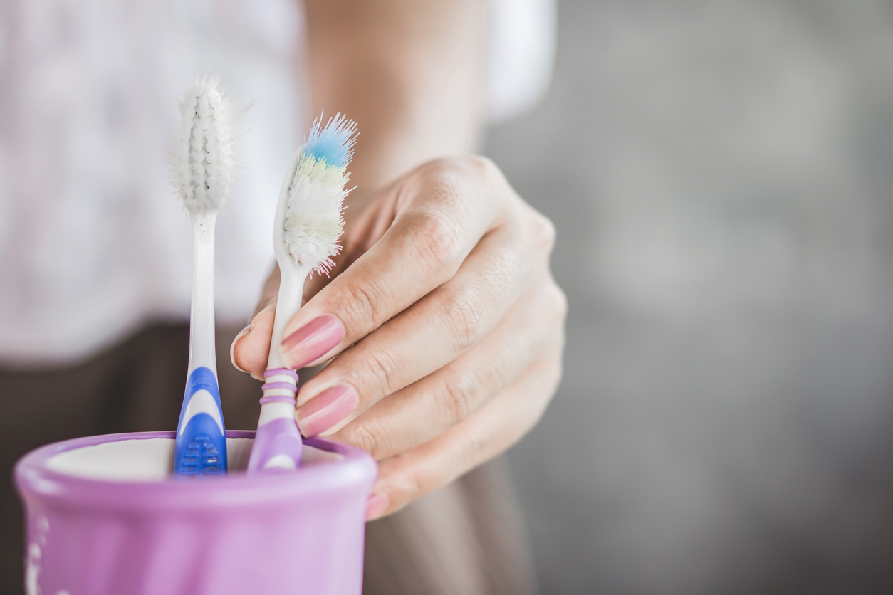 close view of two toothbrushes in jar as a woman's hand picks up one of them