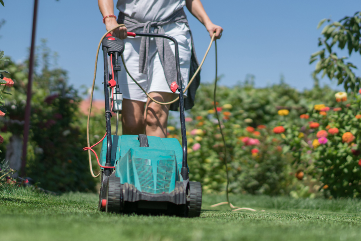 woman mowing the lawn in garden with electric lawn mower