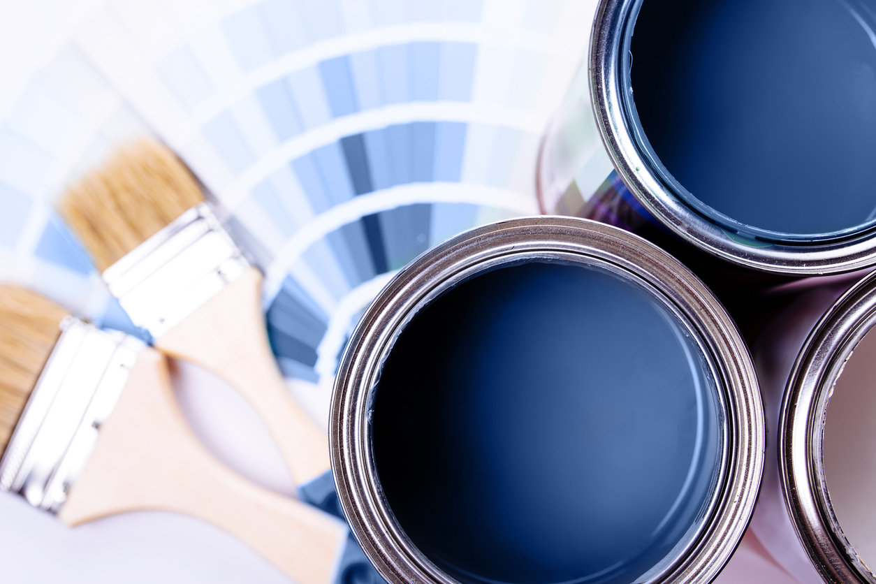 overhead view of open paint cans with blue paint inside and blue paint sample sheets fanned out with paint brushes