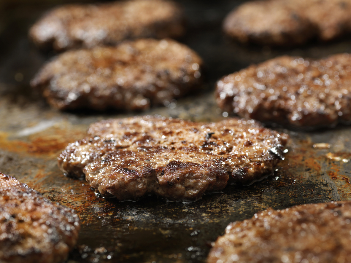 close view of several hamburger patties cooking on griddle