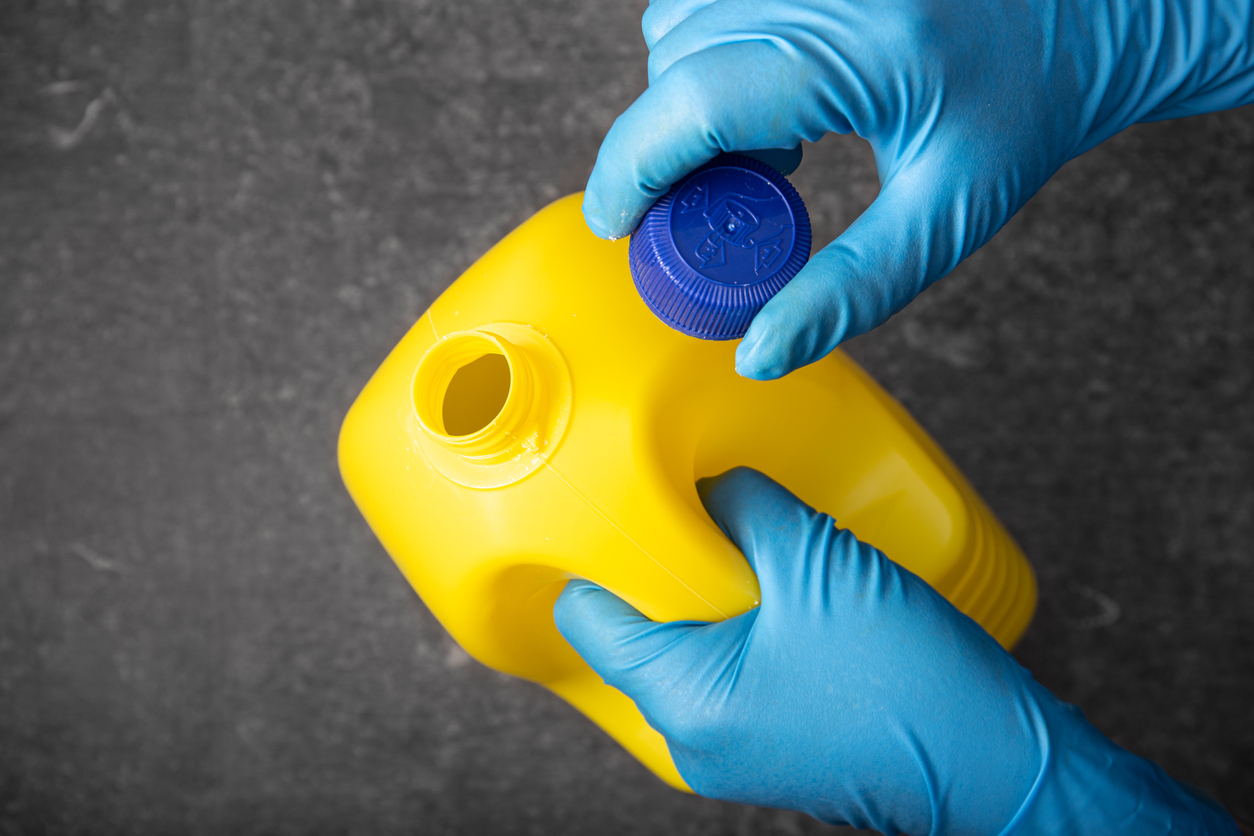 overhead view of gloved hands removing blue cap from yellow bottle of bleach