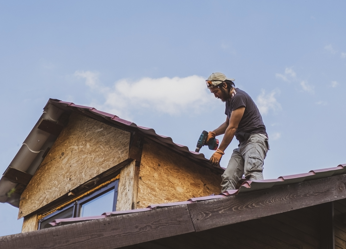 Man working on roof using electric screwdriver.