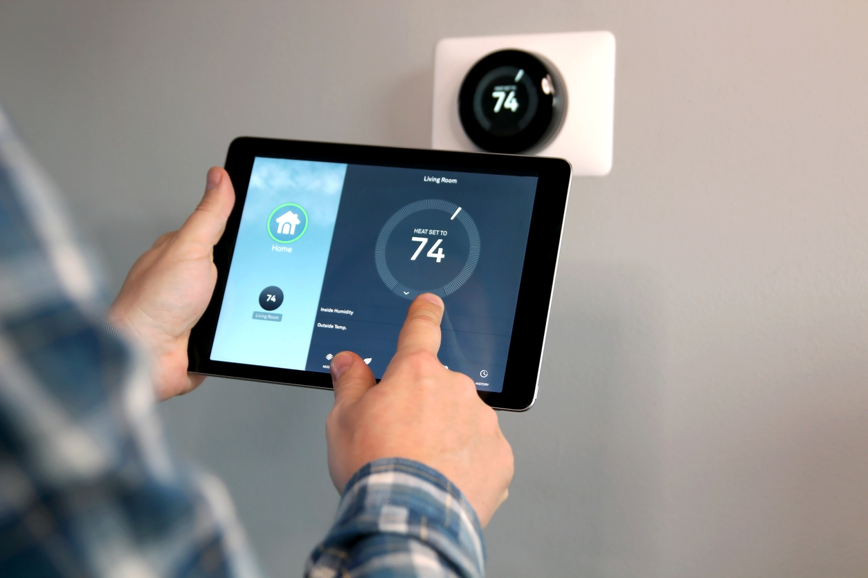man uses an ipad to adjust the smart thermostat on the wall in front of him