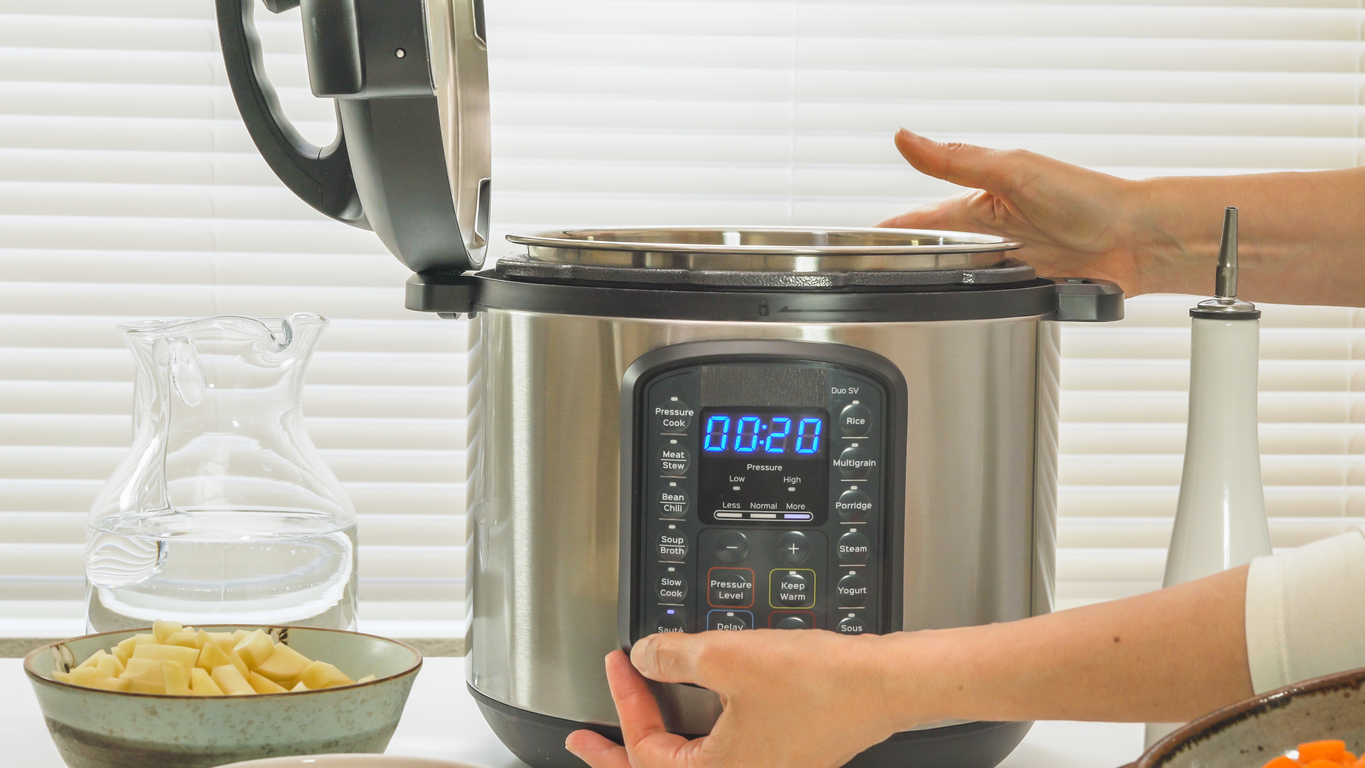 woman's hands setting a pressure cooker on kitchen table with bowls of food next to it